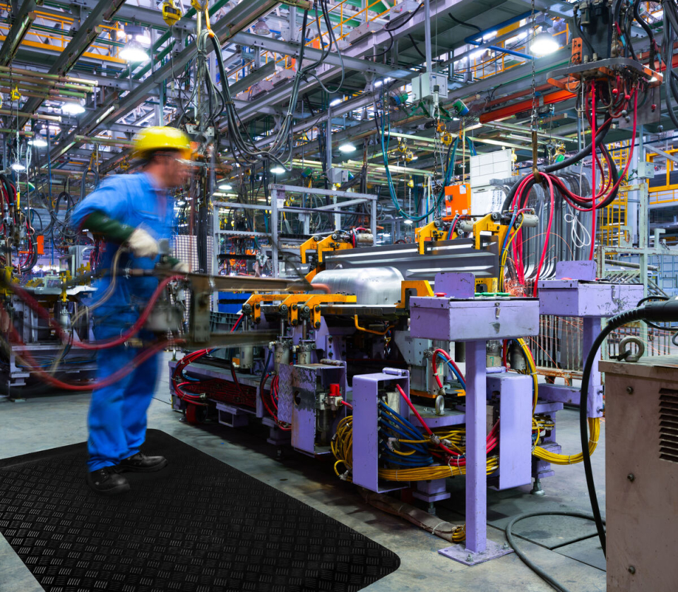 Medarbetare står på en ergonomisk arbetsplatsmatta vid en maskin i industrin